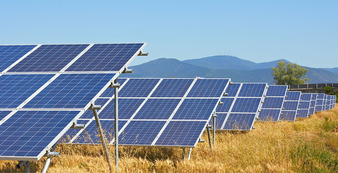 Photograph of a row of solar panels in a field with mountains in the background