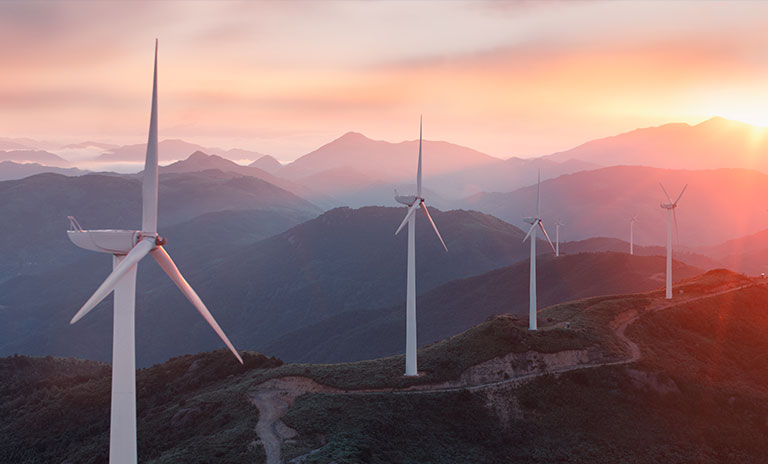 Photograph of many wind turbines on top of mountains with the sun setting in the background
