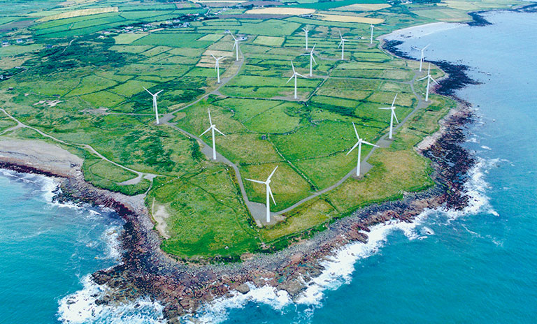 Arial photograph of a shoreline with green fields and wind turbines