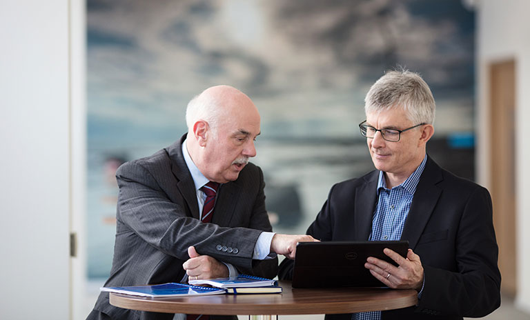 Image of two men in a meeting room sitting side by side and looking at a laptop