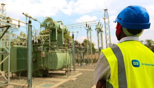 Photograph of a man with his back to the camera. He is wearing a hard hat and a high vis vest with the ESB International logo on it. He is looking at some machinery