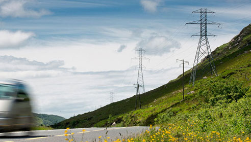 Photograph of electricity pylons on a hill next to a road