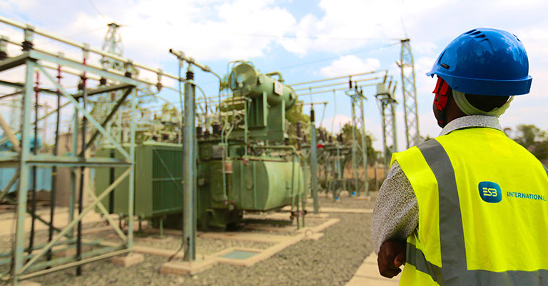 Photograph of a man with his back to the camera. He is wearing a hard hat and a high vis vest with the ESB International logo on it. He is looking at some machinery