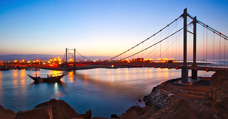 Photograph of a bridge over a river and leading into a city taken at night