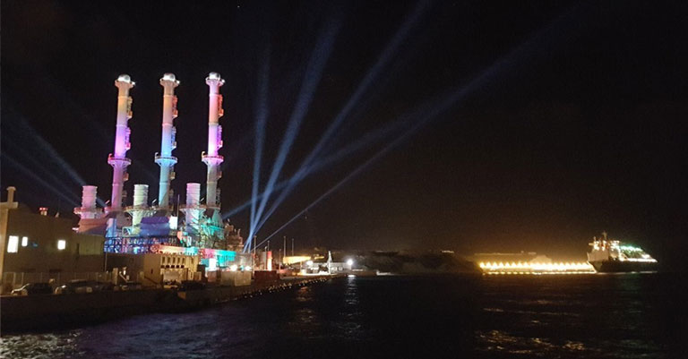 Image of a power station lit up with coloured lights at night time