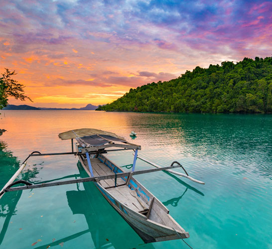Photograph of a wooden boat on a river with forest and a sunset in the background