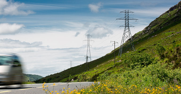 Photograph of electricity pylons on a hill next to a road
