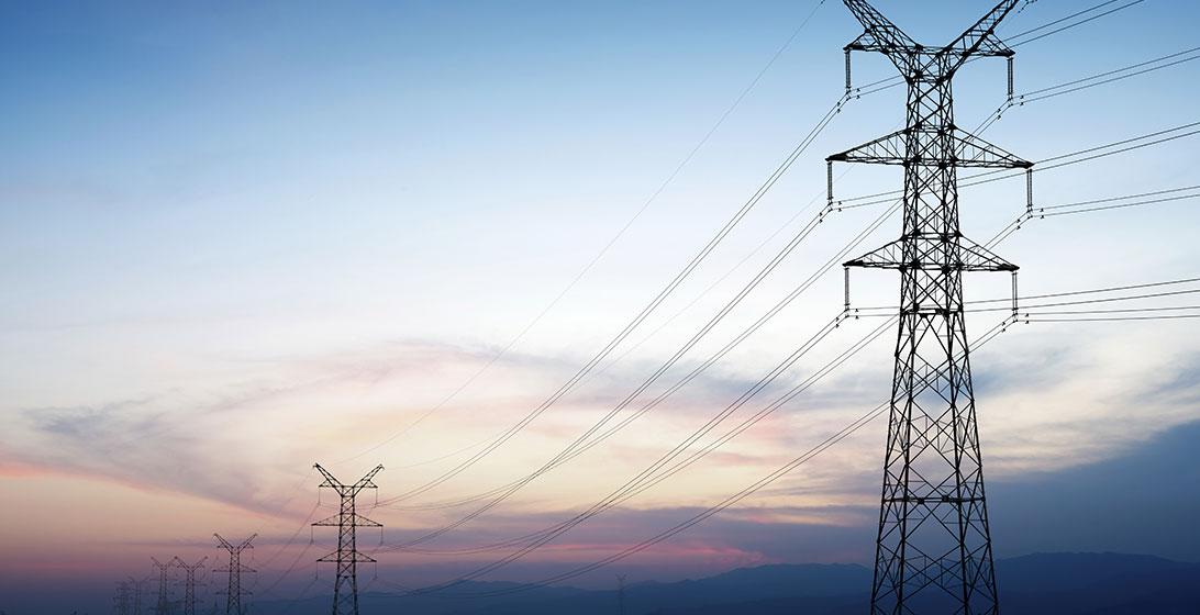 Photograph of electricity wires and pylons against a sunset