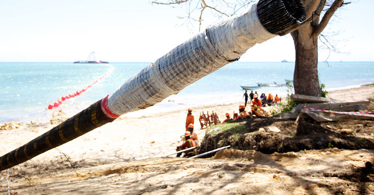 Photograph of a pipe leading onto a beach with workers at the end