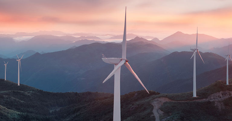 Photograph of a windfarm at the top of some mountains with the sun setting behind
