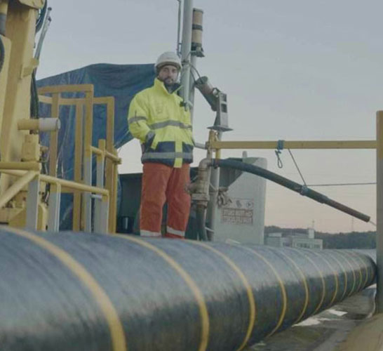 Photograph of a worker on a ship. There is a large cable in the foreground