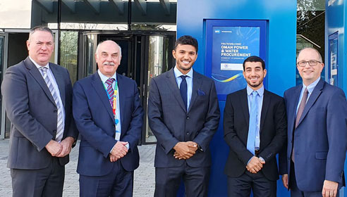 Photograph of five men in suits smiling at the camera. They are standing outside a modern building