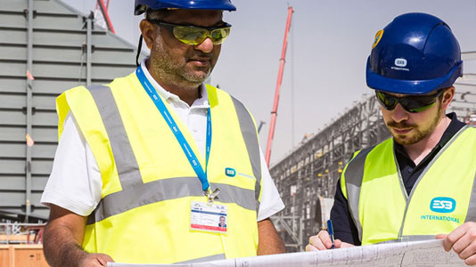 Image of two men in high vis vests and hard hats looking at some drawings on a building site