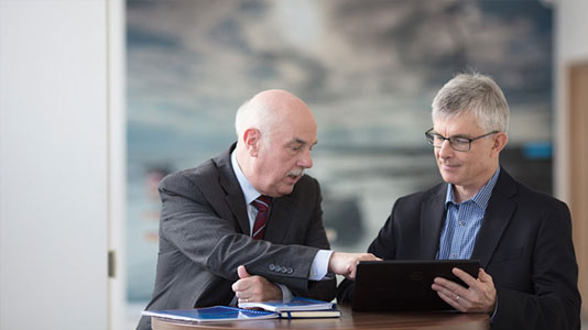 utility-to-utility-staggard-card Image of two men in a meeting room sitting side by side and looking at a laptop