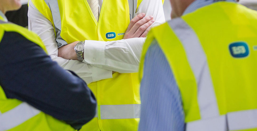 Close up photograph of a mans chest. He is crossing his arms and is wearing a high vis vest on top of a shirt and tie